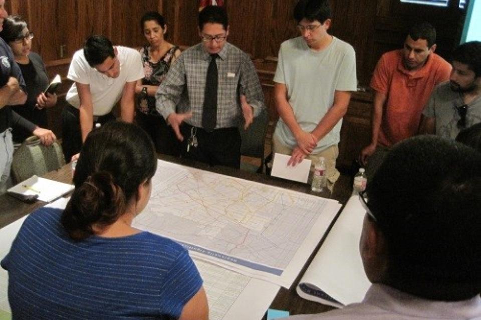 Group discusses a large map spread on a table in an office setting.