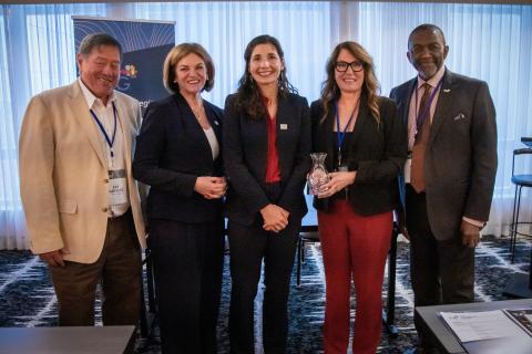 Five people smiling and posing in a conference room.